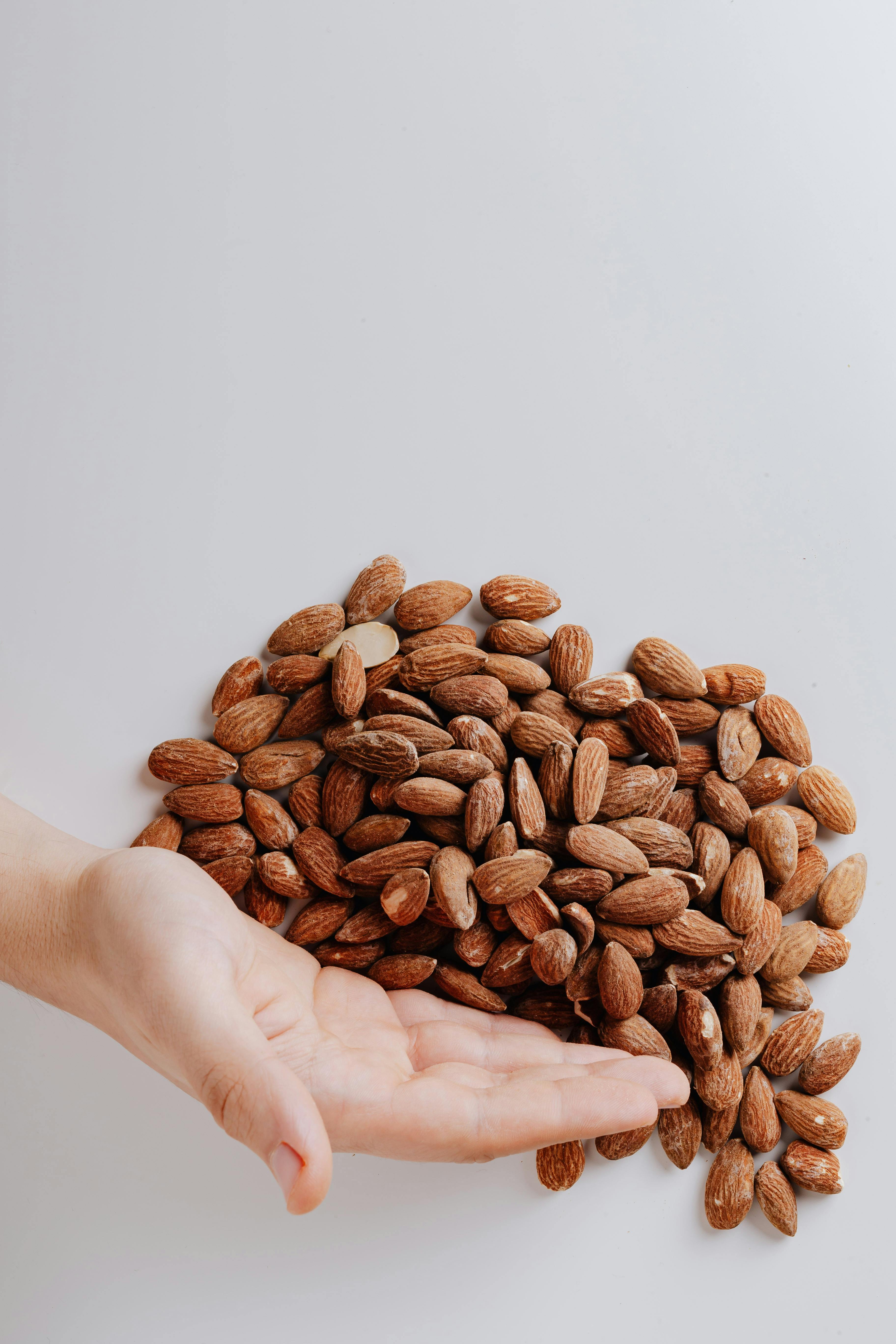 Close-up of a hand with raw almonds on a white background, emphasizing healthy food options.